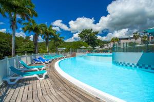 a pool at a resort with blue chairs and palm trees at Karibea Sainte Luce Hotel in Sainte-Luce