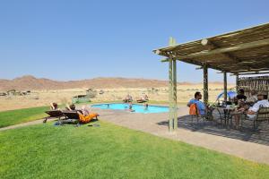 eine Gruppe von Menschen, die um einen Pool herum sitzen in der Unterkunft Sossus Oasis Campsite in Sesriem