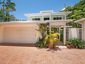 a white house with a garage and palm trees at Reef Villa Port Douglas in Port Douglas