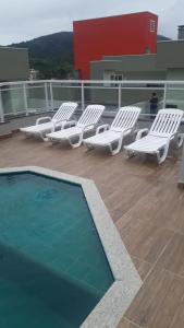 eine Gruppe weißer Liegestühle und ein Swimmingpool in der Unterkunft Vila Monrealle in Ubatuba