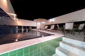 a swimming pool at night with chairs and tables at Apartamento Maceió - De frente a Praia de Jatiuca in Maceió