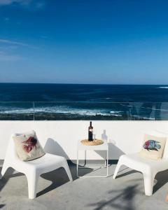 2 sillas blancas y una mesa con una botella de vino en CASA ANCLADA en LA SANTA- 4 Apartamentos frente al mar- 1ª linea solarium barbacoa, en La Santa