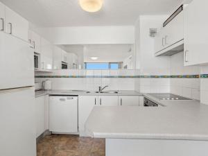 a white kitchen with white cabinets and a sink at Ebbtide 38 On The Beach in Forster