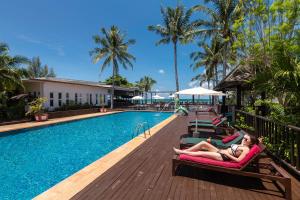 a woman laying on lounge chairs next to a swimming pool at Nakara Long Beach Resort - SHA Extra Plus in Ko Lanta