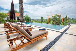 a villa with a pool with chairs and an umbrella at Paradise Luxury Exceptional Staff Lebah Villas in Ubud