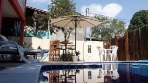 a pool with chairs and an umbrella and a table and chairs at Pousada Semente in Arraial d'Ajuda