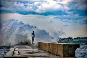 a man standing on a pier in the ocean with a wave at Apartments Jurišević in Umag