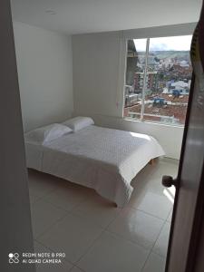 een witte slaapkamer met een bed en een raam bij Hotel Mi Gloria in Tunja