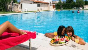 Due donne sedute accanto a una piscina con un cesto di frutta di Masseria Madonna dell'Arco Agriturismo a Martina Franca