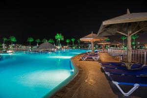 Sunrise Royal Makadi Resort في الغردقة: مسبح في الليل مع كراسي ومظلات