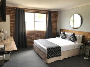 1 dormitorio con 1 cama grande y pared de ladrillo en Coffs Shearwater Motel, en Coffs Harbour