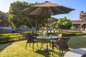 a table with chairs and an umbrella in the grass at StayVista at Dudly Manor with Swimming Pool in Dehradun