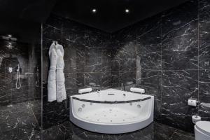 a black tiled bathroom with a tub and a toilet at H Hotel & SPA - Adults Only in St. Julianʼs