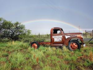 an old truck sitting in a field with a rainbow in the background at Denmark Farm Stay in Cradock