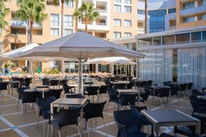 un patio con mesas, sillas y una sombrilla en Hotel Neptuno by ON GROUP, en Roquetas de Mar