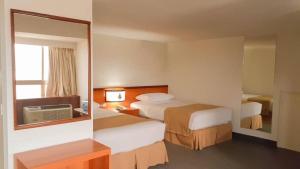 a hotel room with two beds and a mirror at Hotel Cristina Suites in Puerto La Cruz