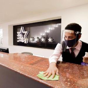 Hotel Cristina Suites في Puerto La Cruz: رجل يلبس قناع الوجه وينظف كاونتر