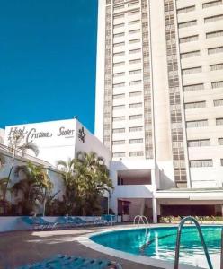 a swimming pool in front of a hotel with tall buildings at Hotel Cristina Suites in Puerto La Cruz