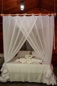 a bed with white curtains and roses on it at Pousada Bahia-Nova Caraíva in Caraíva