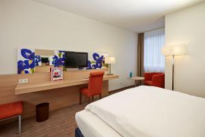 a hotel room with a bed and a desk with a tv at H+ Hotel Wiesbaden Niedernhausen in Niedernhausen