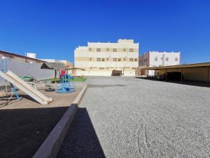 um parque de estacionamento vazio com um edifício e um parque infantil em Salassel Al Jabal Al Akhdar Guesthouse em Al ‘Aqar