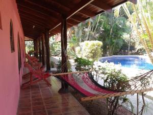 a hammock on the porch of a house with a pool at Hotel El Paraiso Escondido - Costa Rica in Jacó