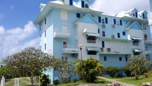 un bâtiment bleu et blanc avec des arbres devant lui dans l'établissement Appartement d'une chambre avec vue sur la mer piscine partagee et balcon amenage a Sainte Anne a 1 km de la plage, à Sainte-Anne