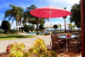 um pátio com uma mesa com um guarda-sol vermelho e cadeiras em 6 bedrooms villa with sea view private pool and wifi at Loule em Loulé