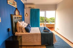 a bedroom with a bed with blue walls and a window at L'escalier Cabanas 107 in Amanzimtoti