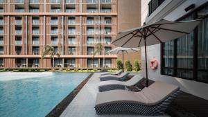 een zwembad met stoelen en een parasol naast een gebouw bij Mandarin Eastville, Pattaya - SHA Extra Plus in Noord Pattaya