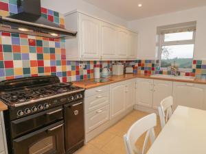 a kitchen with white cabinets and a stove and a table at Hen Stabl in Llanrwst