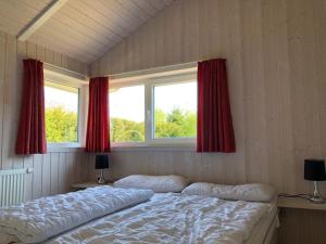 a bedroom with a bed and two windows with red curtains at Strandhus - Haus 37 in Grömitz