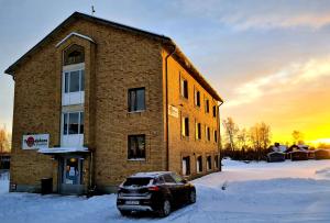 un coche aparcado frente a un edificio de ladrillo en la nieve en Tornedalens B&B en Övertorneå