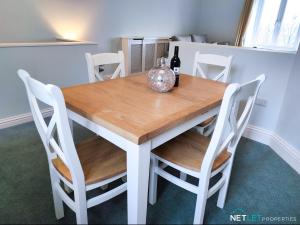 una mesa de madera con sillas blancas y una botella de vino en Station Cottage, en Neyland