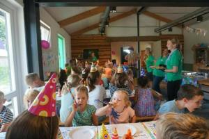 een groep kinderen die verjaardagshoeden dragen en taart eten bij 4-persoons Familielodge in Voorthuizen