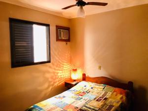 a bedroom with a bed with a ceiling fan and a window at Lindo apartamento 200 metros da praia! in Ubatuba