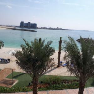 a beach with palm trees in front of the water at 2 Bedroom Deluxe Beach Apartment Al Marjan in Ras al Khaimah