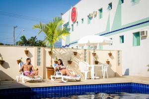 Un hombre y una mujer sentados en sillas de jardín junto a una piscina. en Hotel do Sol Executive, en São Sebastião