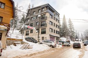 een gebouw in een besneeuwde straat met auto's geparkeerd in de sneeuw bij Apartman Amsterdam Jahorina in Jahorina