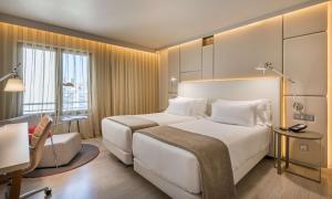 a hotel room with a large white bed and a chair at NH Collection Lisboa Liberdade in Lisbon