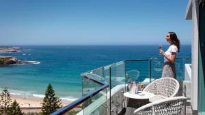 kobieta stojąca na balkonie z widokiem na plażę w obiekcie Crowne Plaza Sydney Coogee Beach, an IHG Hotel w mieście Sydney