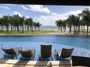 una piscina con sillas, palmeras y el océano en Riviera Beach Place - Aquiraz Riviera, en Fortaleza