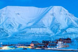 a snow covered mountain with a town in front of a city at Haugen Pensjonat Svalbard in Longyearbyen