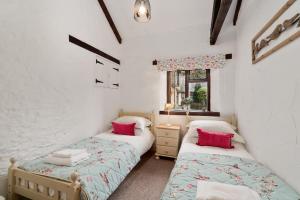 two beds in a room with white walls and red pillows at Daisy Cottage in Paignton