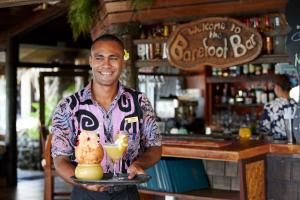 un homme tenant un plateau avec une boisson et un chat sur lui dans l'établissement Pacific Resort Rarotonga, à Rarotonga