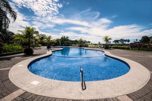 a large swimming pool in a park with palm trees at Ocean View Condo in Los Sueños in Herradura