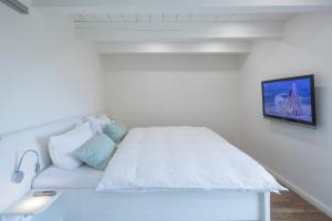 a white bed with pillows and a tv on a wall at Reethus Steuerbord Dagebüll in Dagebüll