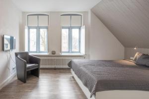 ein Schlafzimmer mit einem Bett und einem Stuhl sowie zwei Fenstern in der Unterkunft Stadthuus 51 in Husum