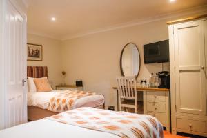 a bedroom with two beds and a desk and a mirror at The Old Fourpenny Hotel in Warwick