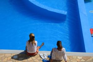 two girls sitting on a bench in front of a swimming pool at Lefkas Petra in Agios Nikitas